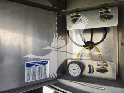 Suspension load scale label and gauge panel inside Mac aluminum flatbed trailer showing pressure gauge and control valves.