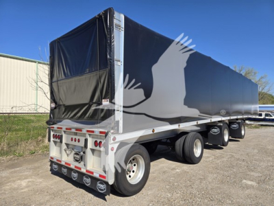 Trailer side view showing Mac aluminum flatbed with black tarpaulin and eagle graphic on silver frame, triple-axle configuration.