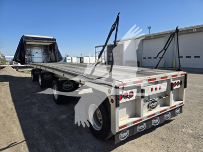 Flatbed trailer showing aluminum deck and fold-down ramps with rear_and_side reflectors and MAC branding. Dual rear wheels, taillights, and mud flaps visible.