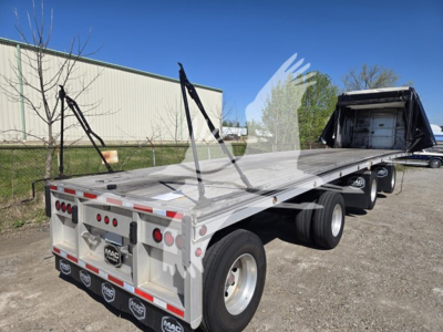 Flatbed trailer showing aluminum deck and side rails with straps, rear bumper and taillights visible, 2023 Mac aluminum flatbed trailer in a used condition.
