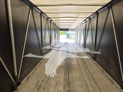 Aluminum flatbed trailer interior with ribbed floor and side rails, long corridor viewpoint toward open end.