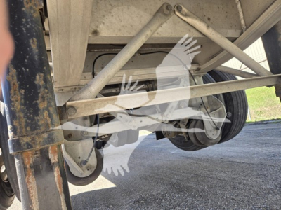 Trailer undercarriage showing suspension frame and axle with wheel hub and leaf springs in a Mac Aluminum flatbed.