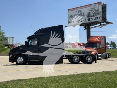 Peterbilt 579 conventional sleeper truck with a black cab and white graphics, attached to a red trailer tractor at a truck lot.