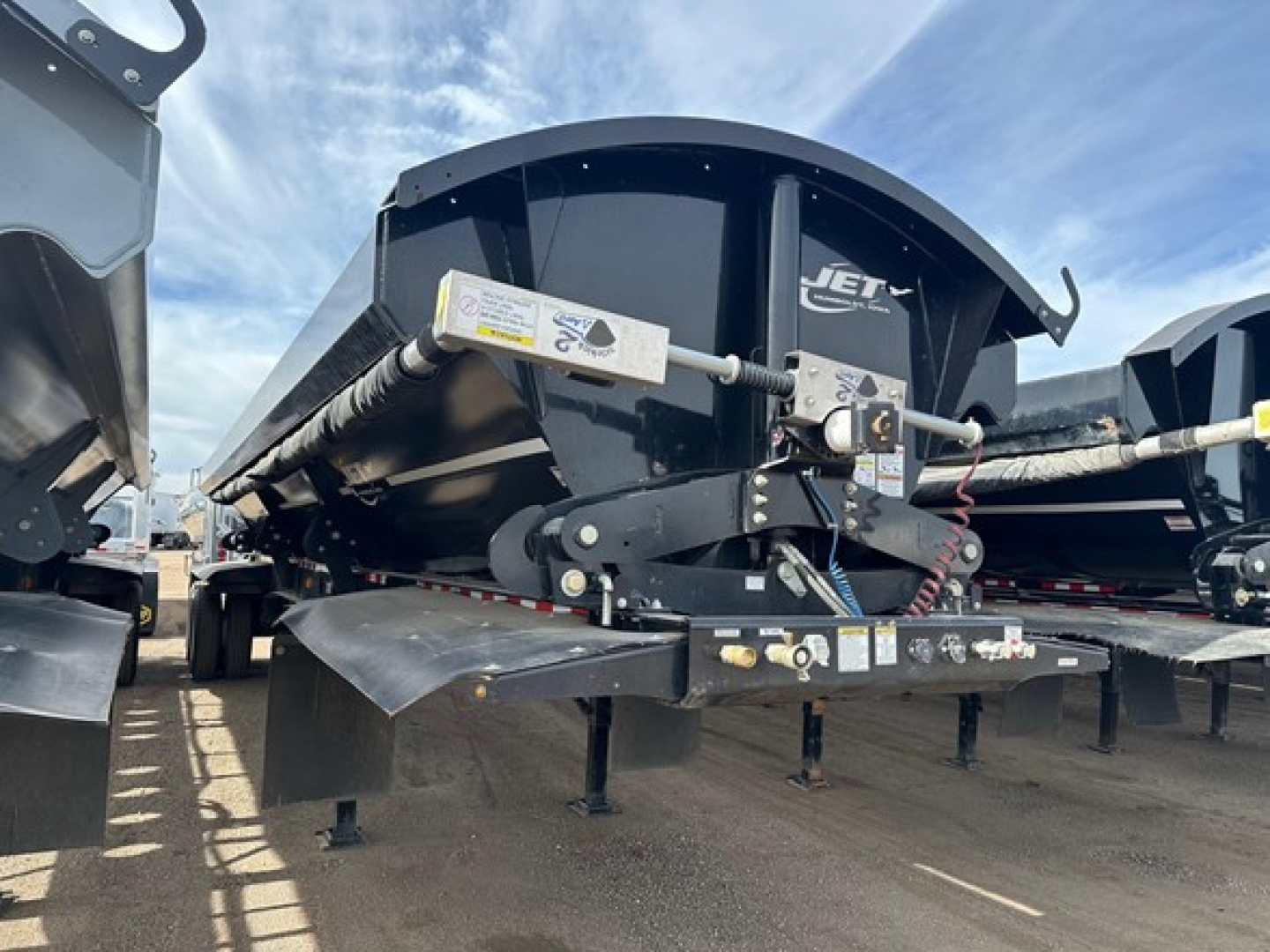 Jet Air Ride Side Dump trailer hitch and mechanisms showing hydraulic actuators and safety decals in a yard.