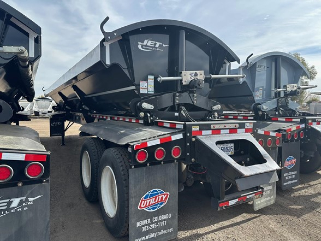 Jet side dump trailer showing hydraulic dump bed and rear bumper with reflective tape, dual axle tires, and Utility Denver Colorado sticker.