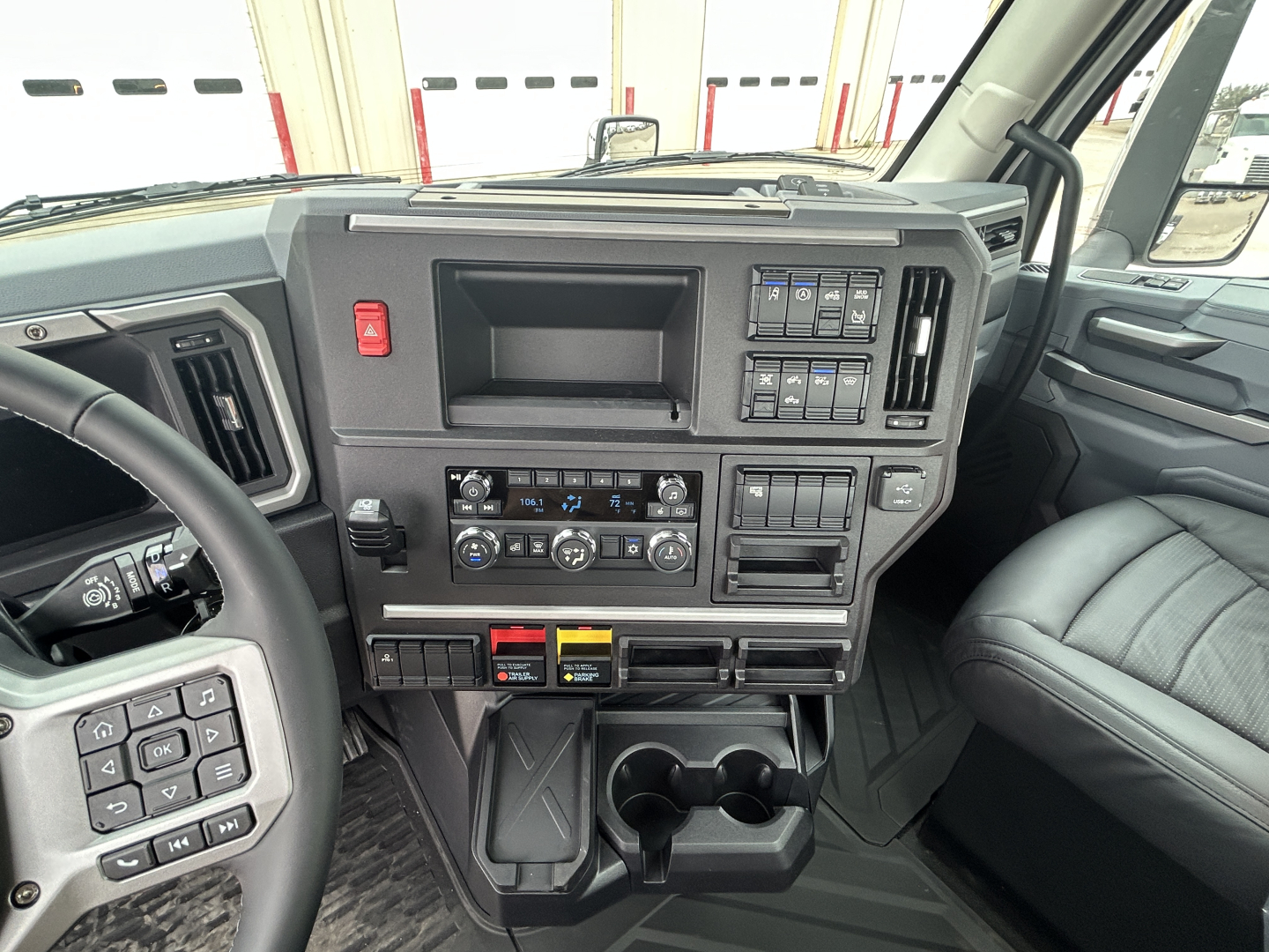Dashboard and center console of a 2027 Mack AN64T tractor cab showing steering wheel, control panel, switches, and cup holders.