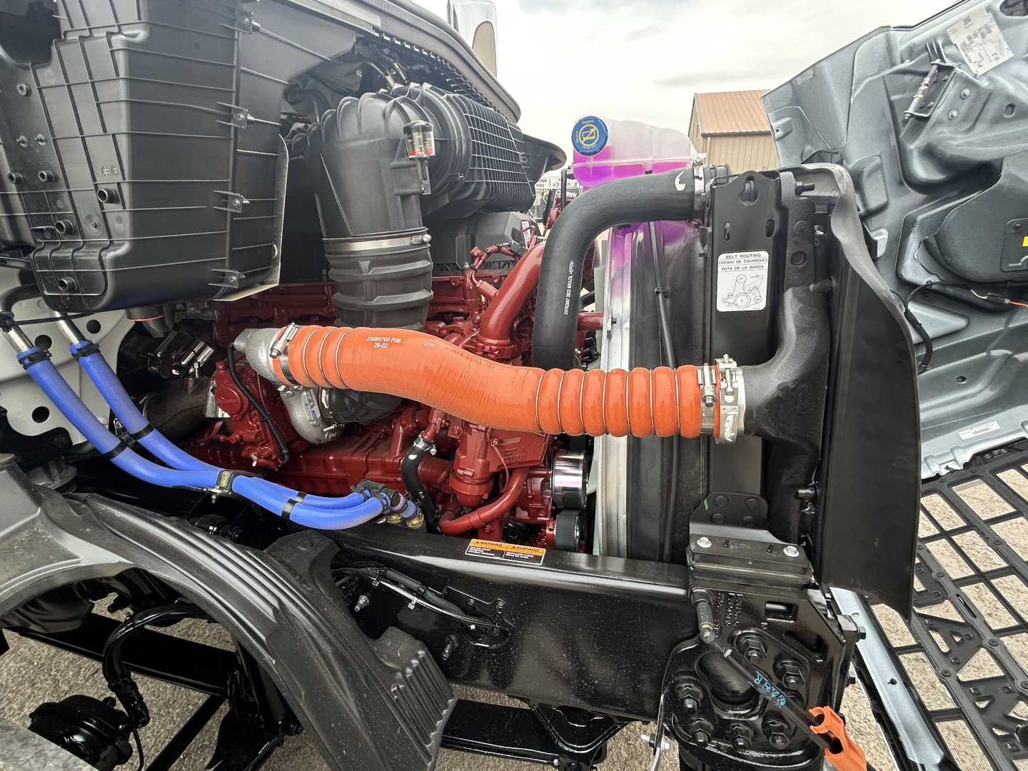 Mack AN64T engine bay showing orange turbo hose, red engine block, blue hoses, and radiator assembly.