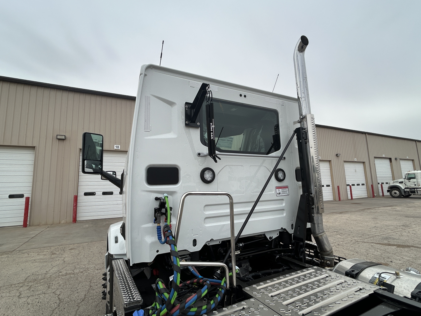 Truck cab rear view showing exhaust stack and steps with braided hoses, white Mack AN64T cab, VIN visible in listing: 1M1A24GY0VM102514.