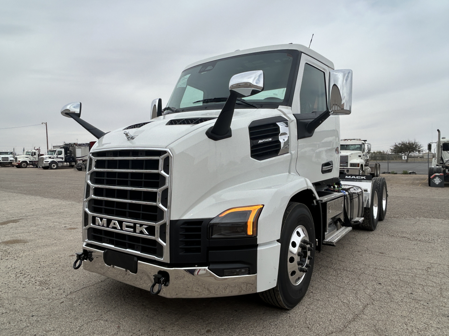Truck front-left view of a white 2027 Mack AN64T conventional daycab with large grille, dual side mirrors, and amber turn signals.