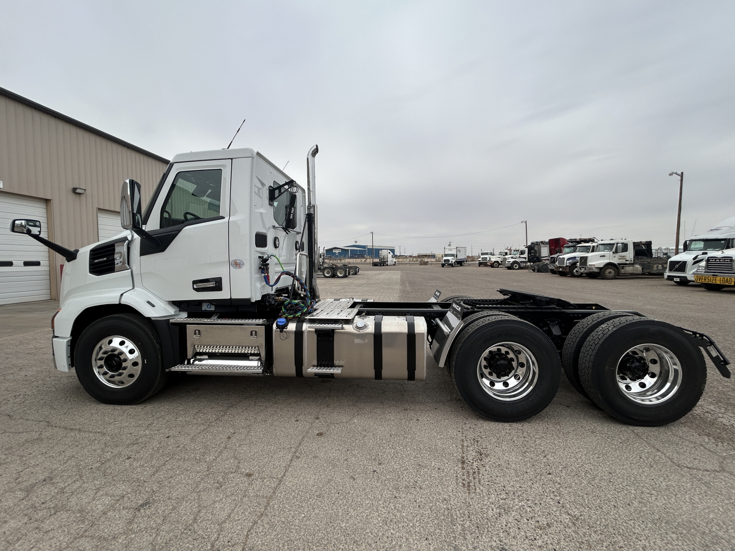 Truck side view showing 2027 Mack AN64T conventional daycab with tri-axle rear and chrome fuel tanks.