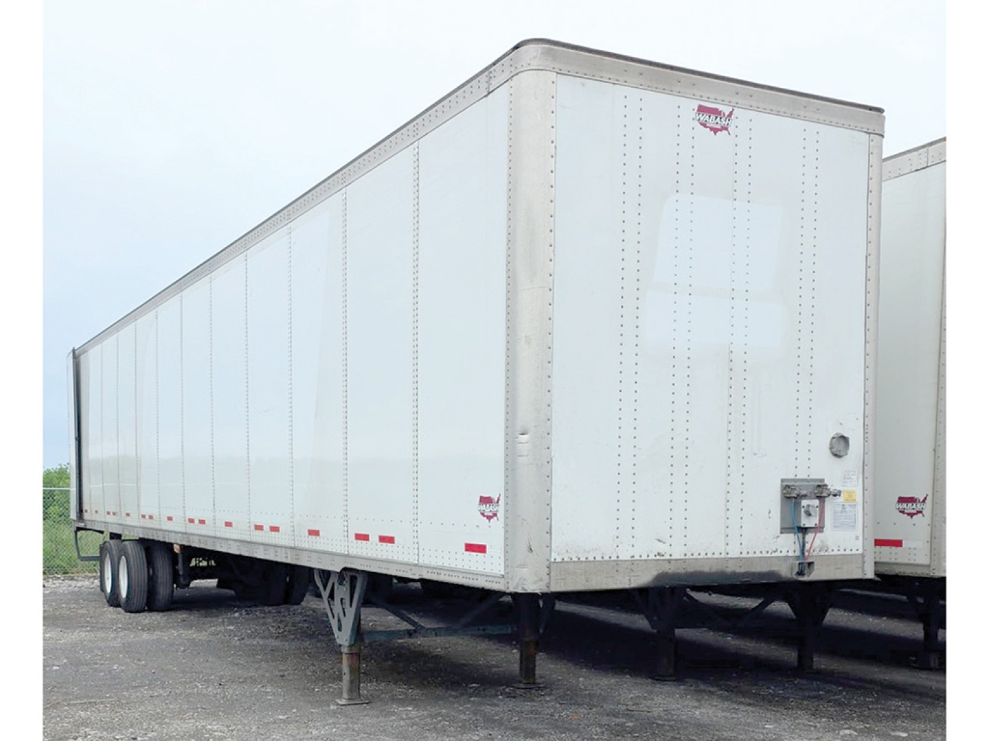 Trailer side and rear showing a white Wabash trailer with tandem axle, pintle stand, and rear bumper. Visible text: none legible; features include reflective tape lines along lower edge.