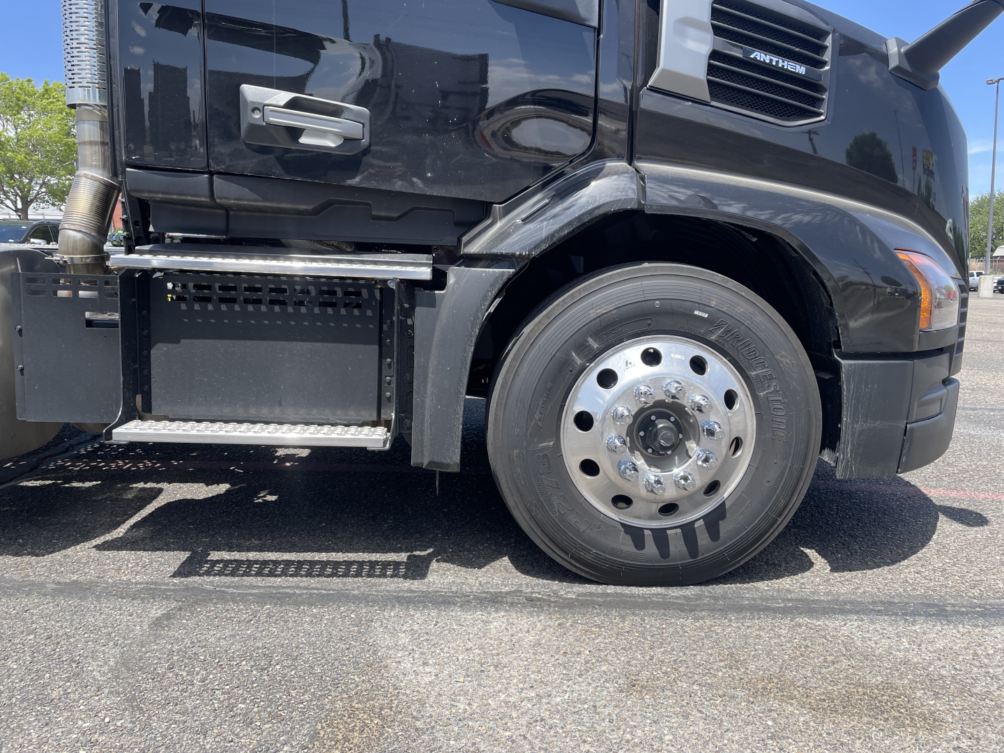 Front left side of a 2027 Mack AN64T conventional daycab truck showing front tire, wheel, and step; visible are chrome hub, side mirror, and part of the cab with WINTONG badge.