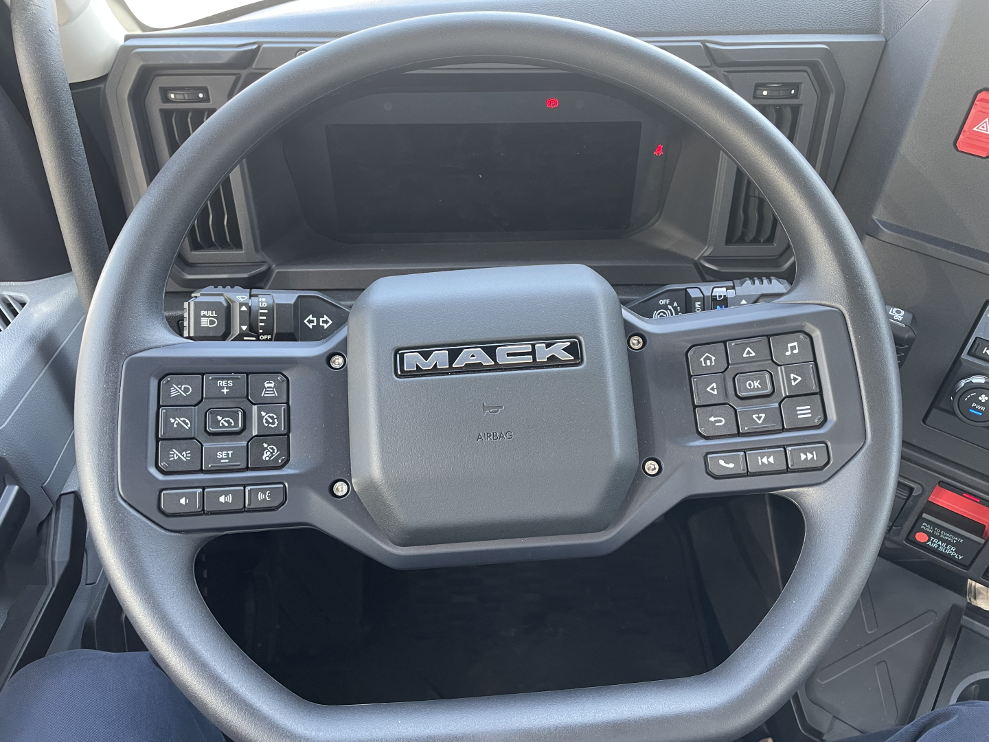 Mack AN64T truck steering wheel with Mack logo and control buttons on both sides visible in cabin interior.