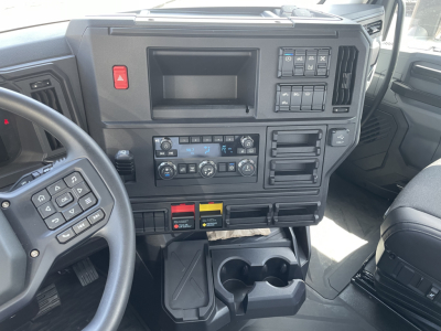 Dashboard of a Mack AN64T cab showing instrument cluster, control buttons, climate controls, and storage compartments; visible text includes hazard button symbol, various switch labels, and cup holders.