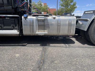 Conventional daycab truck fuel tank and chassis side view showing aluminum cylindrical fuel tank with fuel caps and steps, Mack AN64T branding nearby.