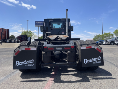 Truck chassis rear view showing dual A-frame connections, mud flaps with Buckner's Truck & Equipment logos, and rear underrun protection on a Mack truck in a lot.