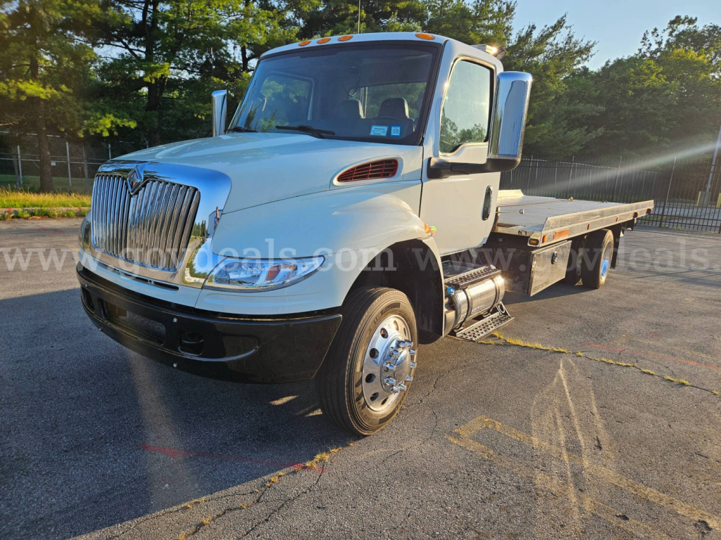 International MV607 tow truck showing front-left view with chrome grille, dual rear wheel, flatbed body, and side mirrors.
