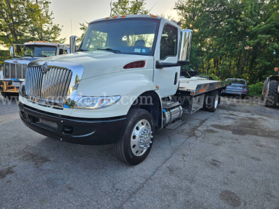 International MV607 tow truck in service showing front grille, cab, and flatbed body with chrome wheels and dual exhaust.
