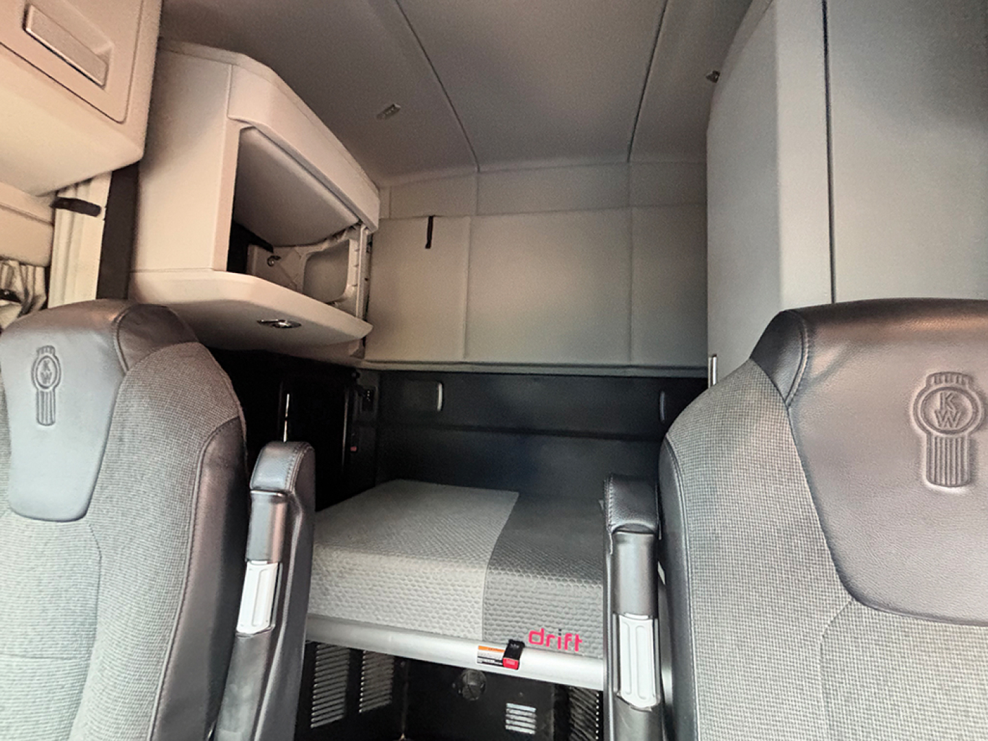 Kenworth T-680 Next Gen cab interior featuring a sleeper berth and overhead storage with two front seats and a bed area visible.