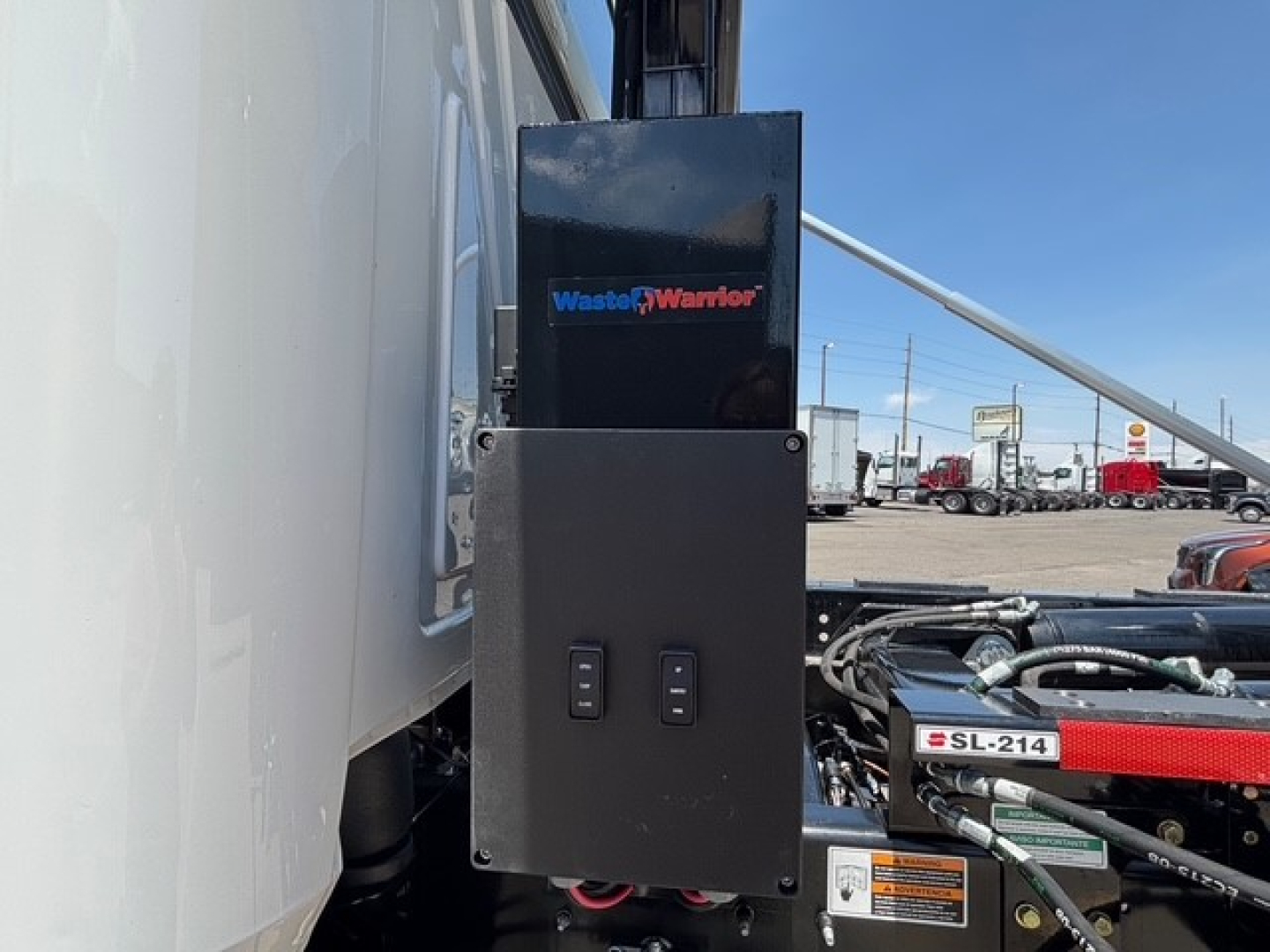 Truck engine bay area showing control box and Waste Warrior branding on a Mack MD7 hooklift truck.