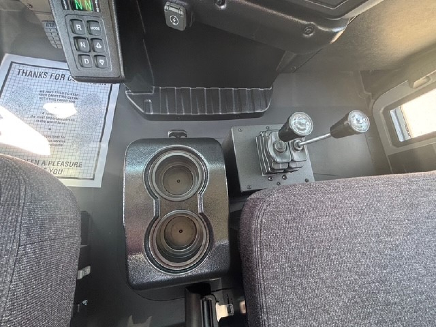 Cab interior of a 2026 Mack MD7 showing center console with circular cup holders, gear shifter, and dashboard controls; part of the driver’s area visible.