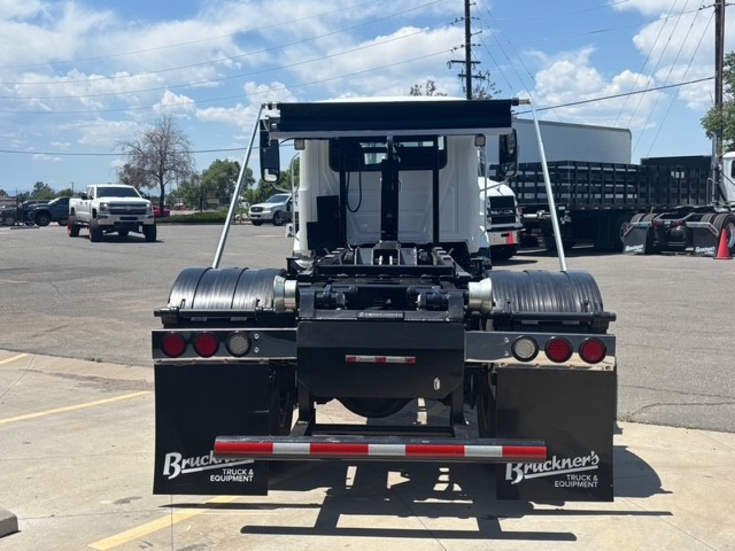 Mack MD7 hooklift truck rear view showing dual rear fenders and hitch assembly with branding plates and taillights.