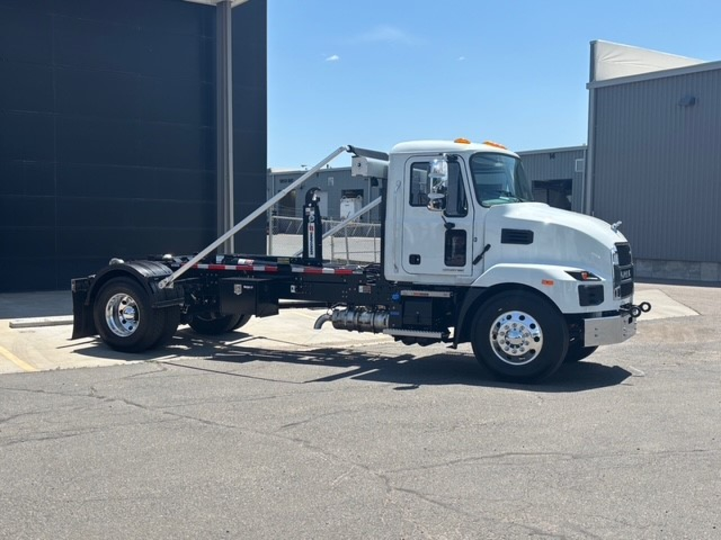Mack MD7 hooklift truck side view showing cab, chassis, and hooklift arm assembly with white paint and chrome wheels.