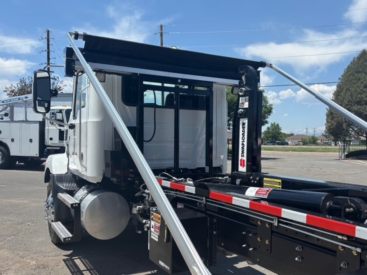 Mack MD7 hooklift truck cab area with extended hydraulic hoist and frame showing white cab and black chassis.