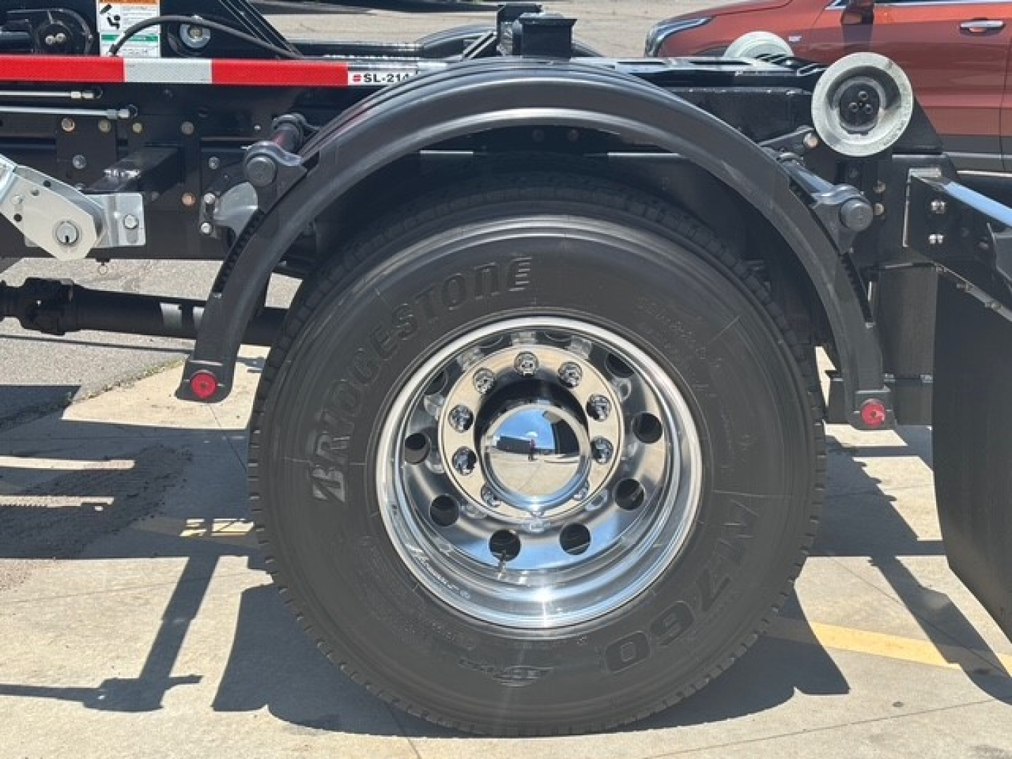 Mack MD7 truck wheel close-up showing VICTORY? tire with chrome rim and hubcap, part of Hooklift setup.