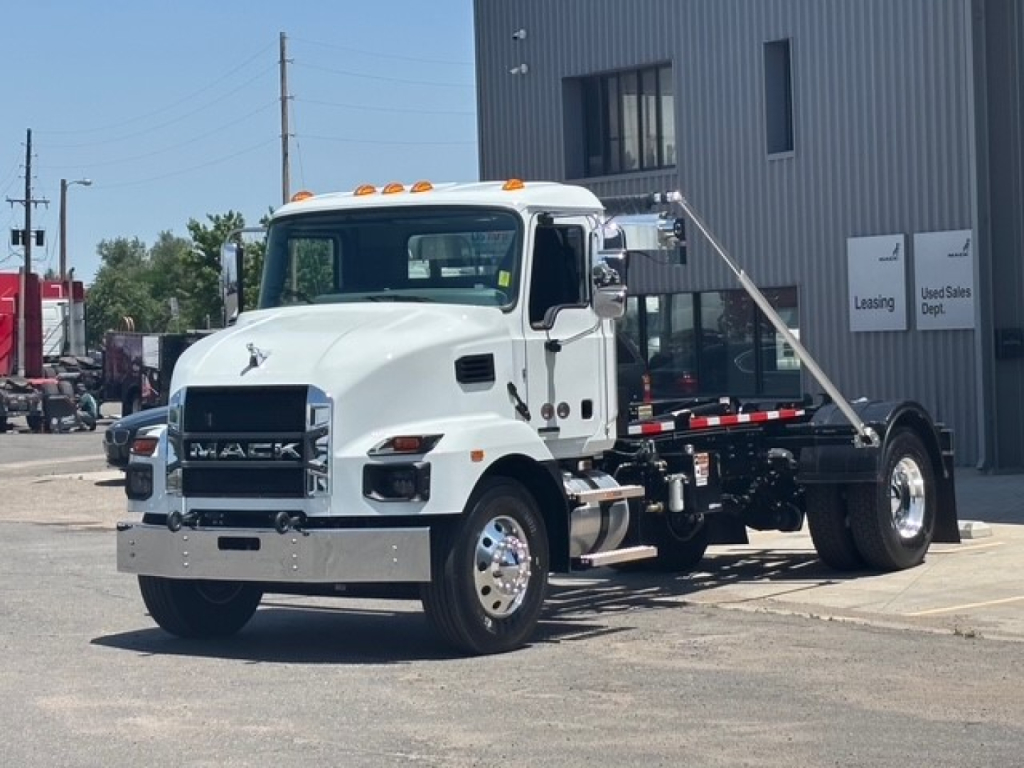 White Mack MD7 hooklift truck in a dealership lot showing front grille with MACK emblem, cab with orange roof lights, and hooklift chassis.