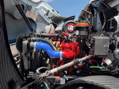 Mack MD7 engine bay showing blue coolant hose, red engine block, and various components with orange cap and gauge in view.