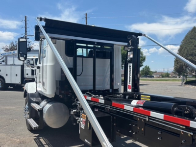 Mack MD7 hooklift truck cab area with extended hydraulic hoist and frame showing white cab and black chassis.