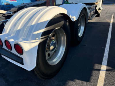 Kenworth T800 rear axle area showing dual rear wheels and white fender with circular taillights in a parking lot.