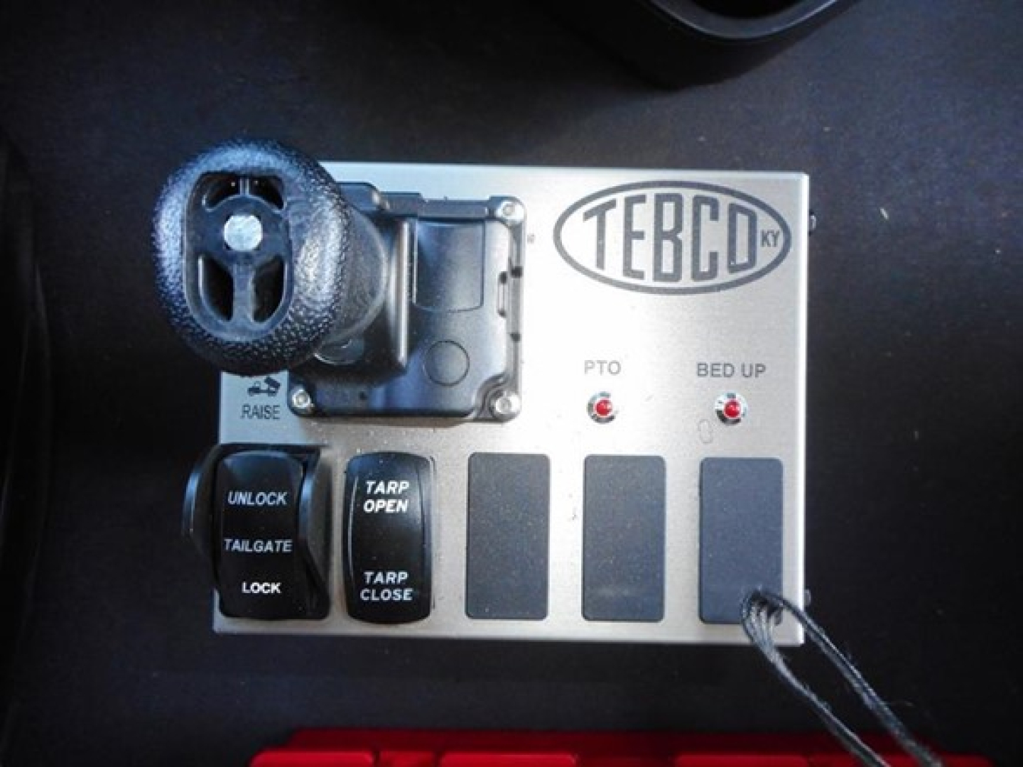 TEBCO control panel with dial, buttons labeled UNLOCK, TARP OPEN/CLOSE, TAILGATE, LOCK and RAISE; Turkish TEBCO logo; black cable attached.