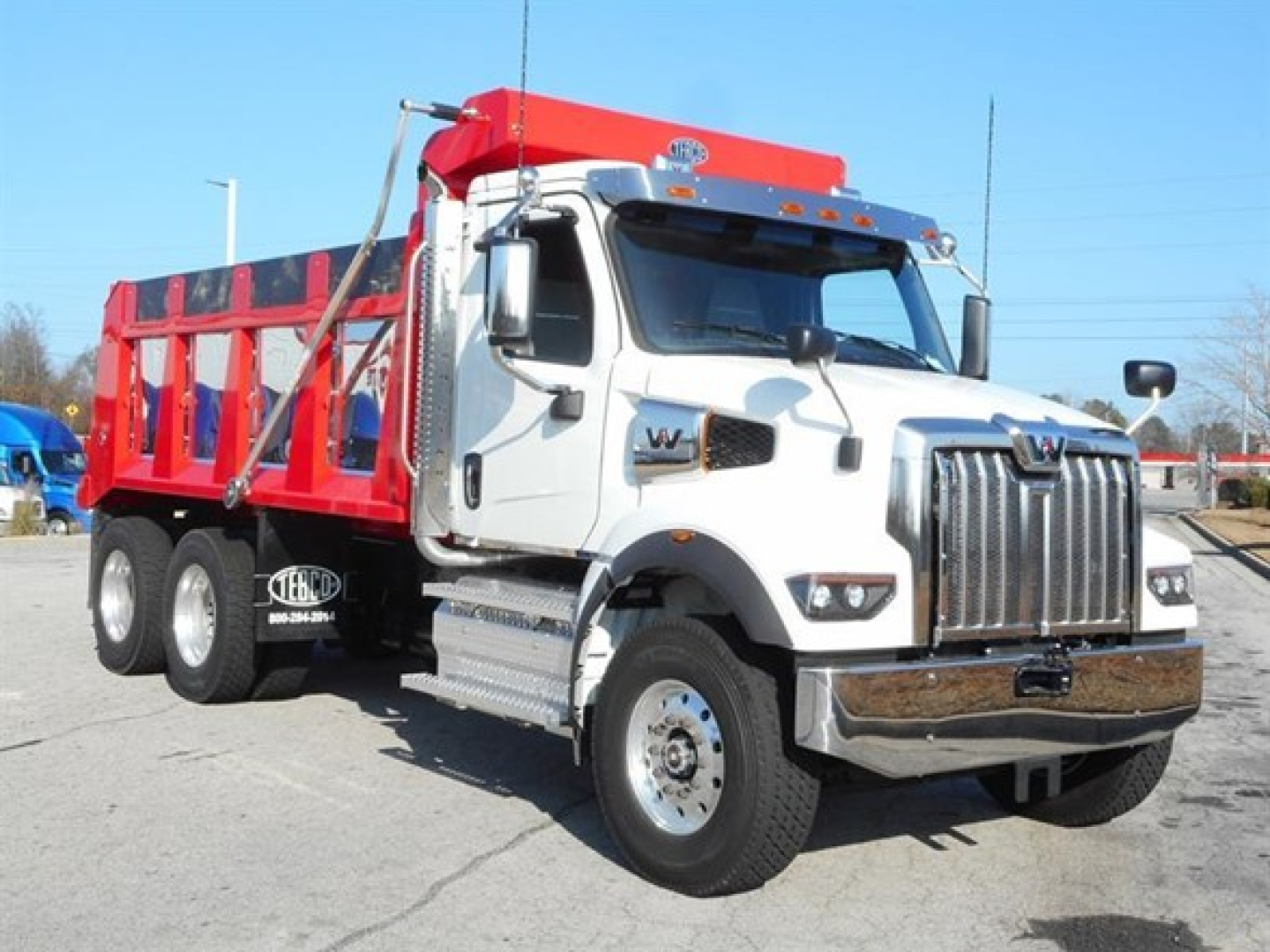 Western Star 47X dump truck with white cab and red dump body, front grille, large mirrors, chrome bumper, and dual rear axles.