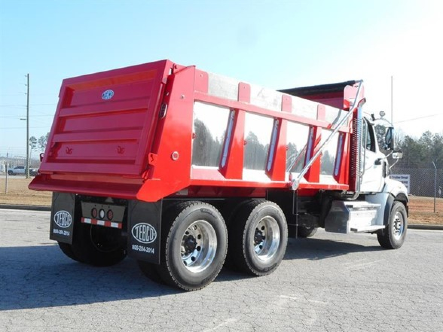Dump truck chassis and cargo bed of a 2026 Western Star 47X with red dump body and white cab, side view showing rear wheels and hydraulic mechanisms.