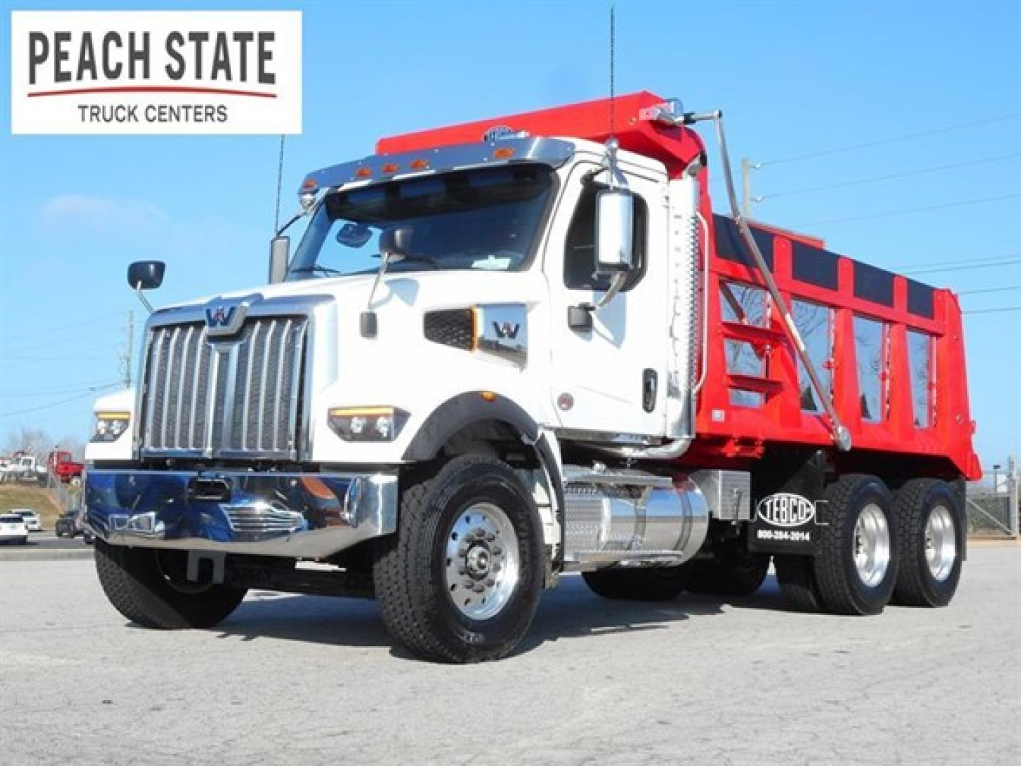 Western Star 47X dump truck in showroom angle showing white cab and red dump body with Peach State Truck Centers logo.