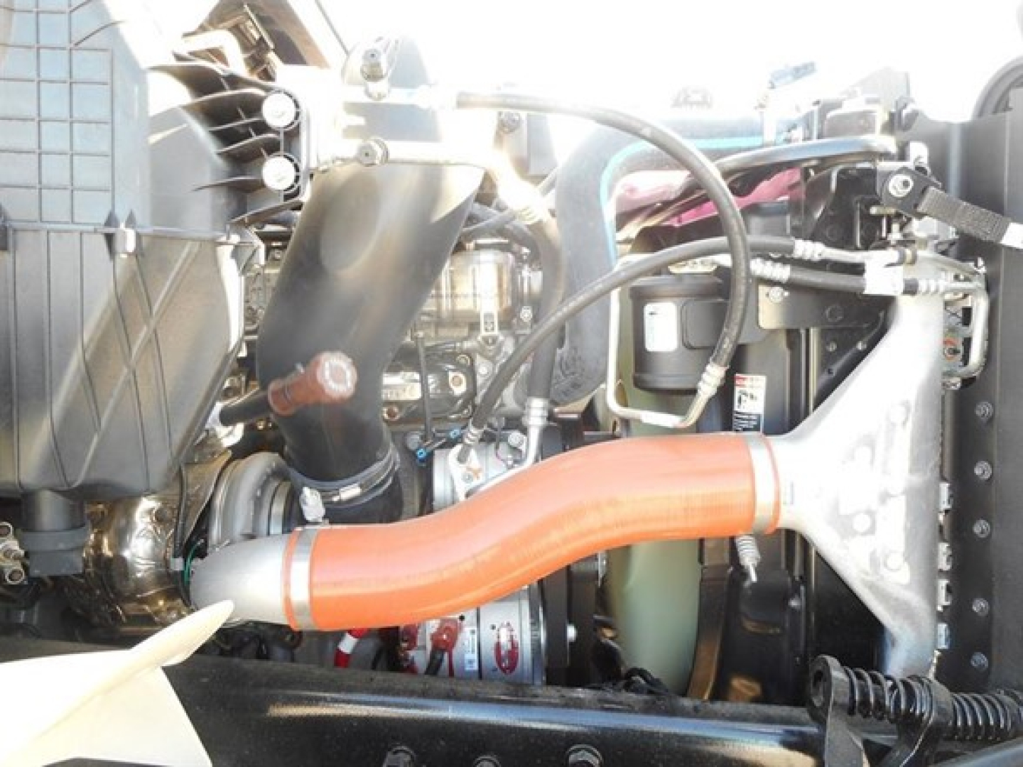Engine bay of a new Western Star 47X dump truck showing orange intake hose, engine components, hoses, and wiring.
