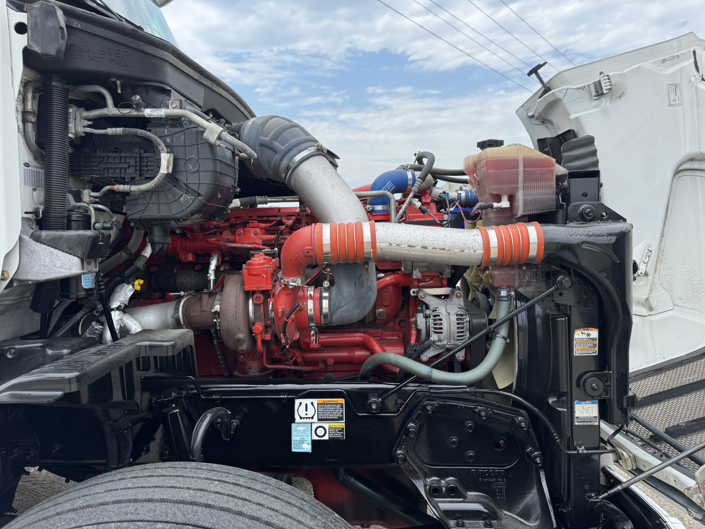 Peterbilt 579 engine bay with red engine and orange intake piping, various hoses and components visible.