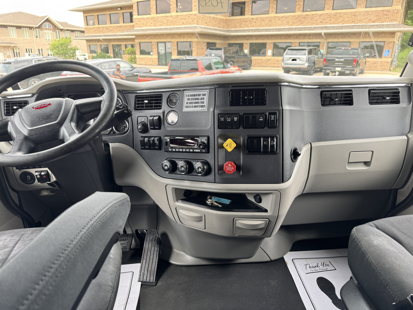 Peterbilt truck interior dashboard view with steering wheel on left, center console controls, gauges, and gear selector. Visible text includes warning label and control markings on the dash.