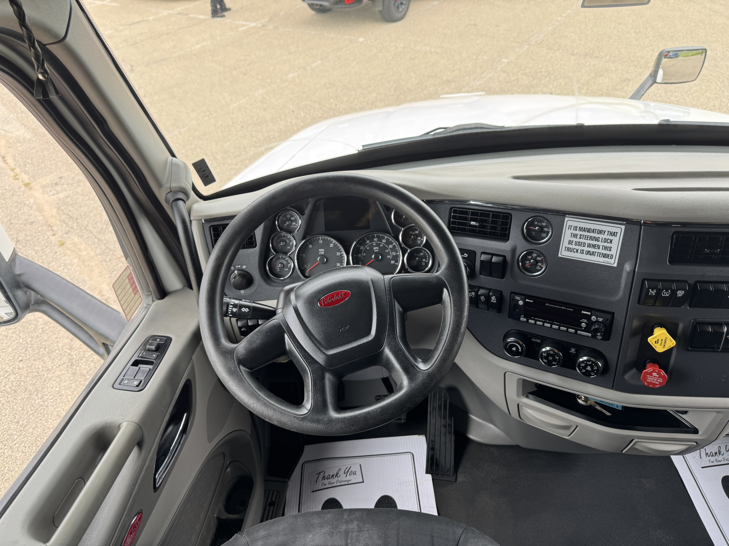 Peterbilt 579 cab interior showing steering wheel with Peterbilt logo, dashboard gauges, and control panel; visible text includes ignition panel labels and sticker details.