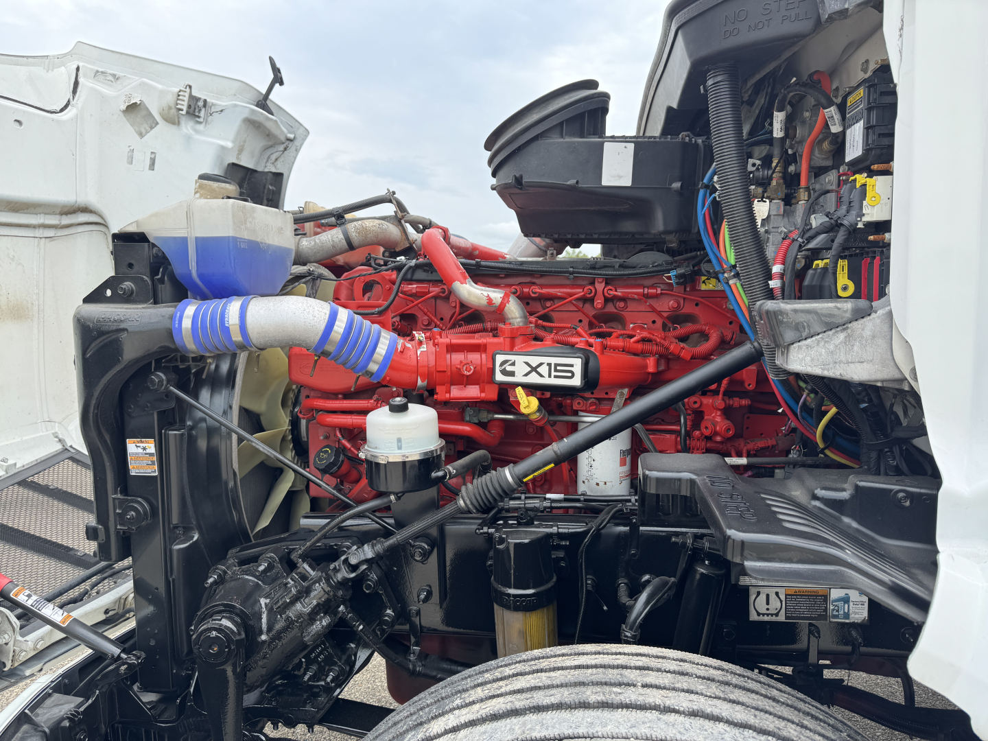 Peterbilt 579 engine bay with red X15 engine visible and various hoses and wiring in the engine compartment.
