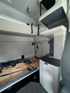Peterbilt cab interior with sleeper area, storage compartments, and dashboard area visible. Includes wood sleeper platform and overhead storage.