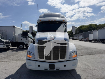 Peterbilt 579 front view showing chrome grille and headlights, white sleeper cab with Peterbilt emblem on grille, trucks lot in background.