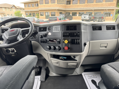 Peterbilt truck interior dashboard view with steering wheel on left, center console controls, gauges, and gear selector. Visible text includes warning label and control markings on the dash.
