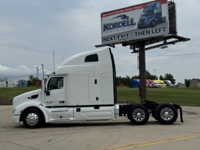 Peterbilt 579 sleeper cab tractor side view with white paint and a billboard in background.