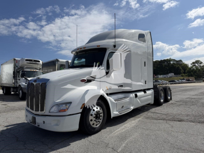 Peterbilt 579 truck in white with sleeper cab, three-axle configuration, front grille and headlights visible, side view of cab and exhaust, outdoor dealership lot.