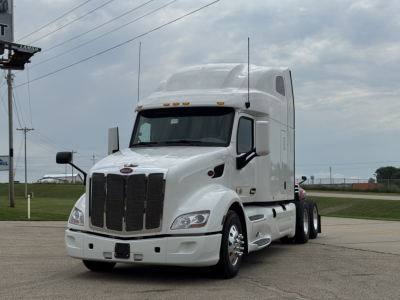 Peterbilt 579 conventional sleeper truck in white, front three-quarter view showing chrome grille, cab, and dual rear axles.