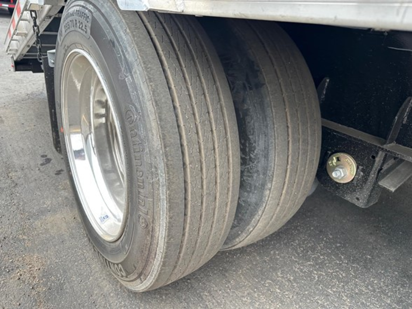 Dual rear tires of a Manac trailer with visible thickness and wheel rim; a portion of the trailer frame and suspension is seen.