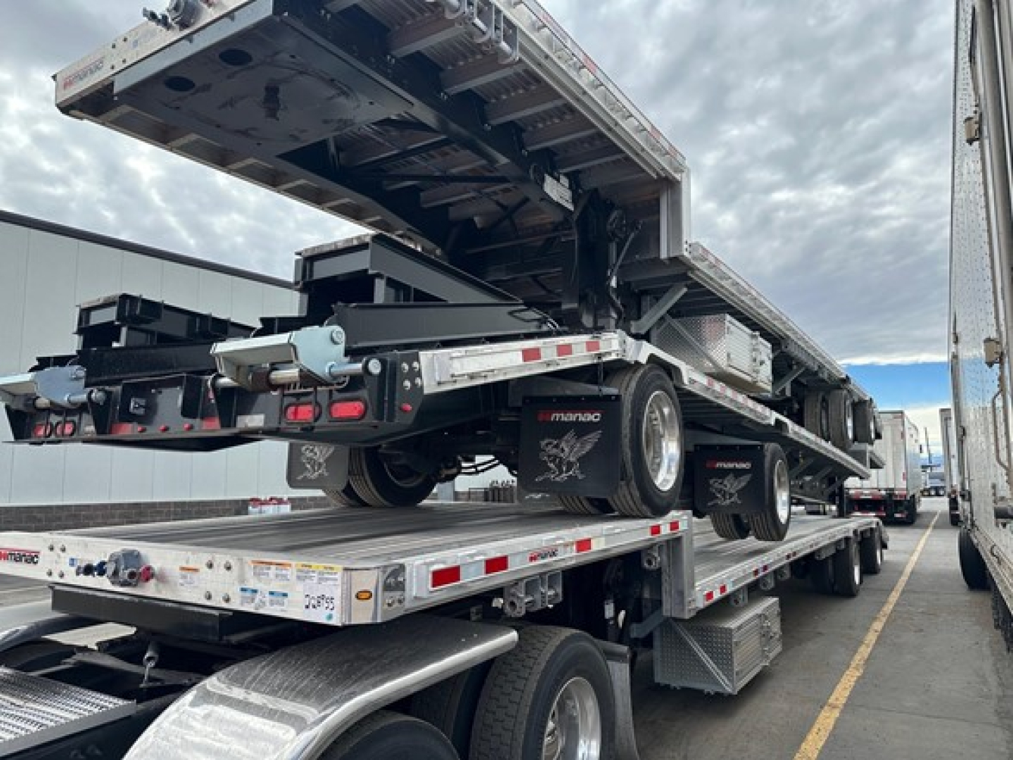 Manac combo drop deck trailer on flatbed truck, rear view showing multiple axles and loading deck, with raised gooseneck and reflective tape.
